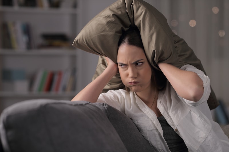 Unhappy woman covering ears with pillow